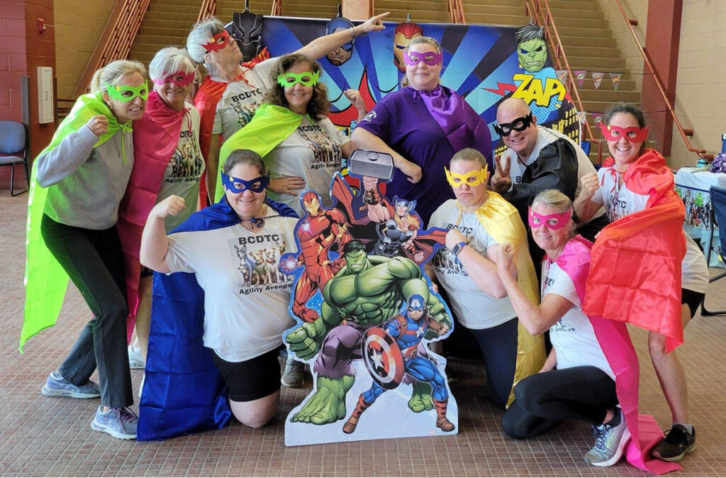 9 women and 1 man dressed in avenger costumes and posing silly