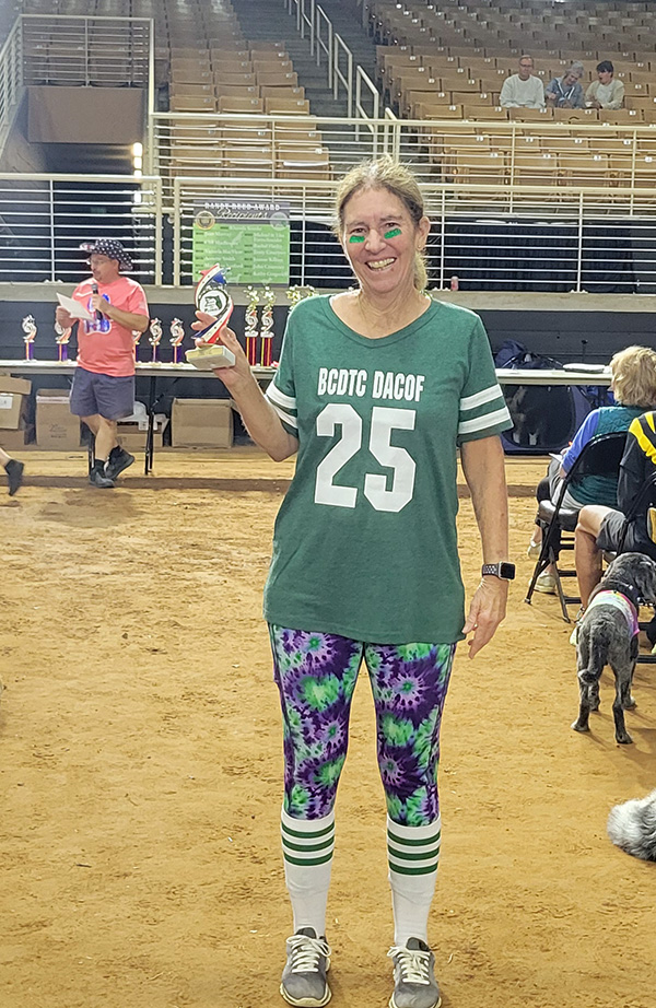 A woman wearing a green football jersey holding a small trophy